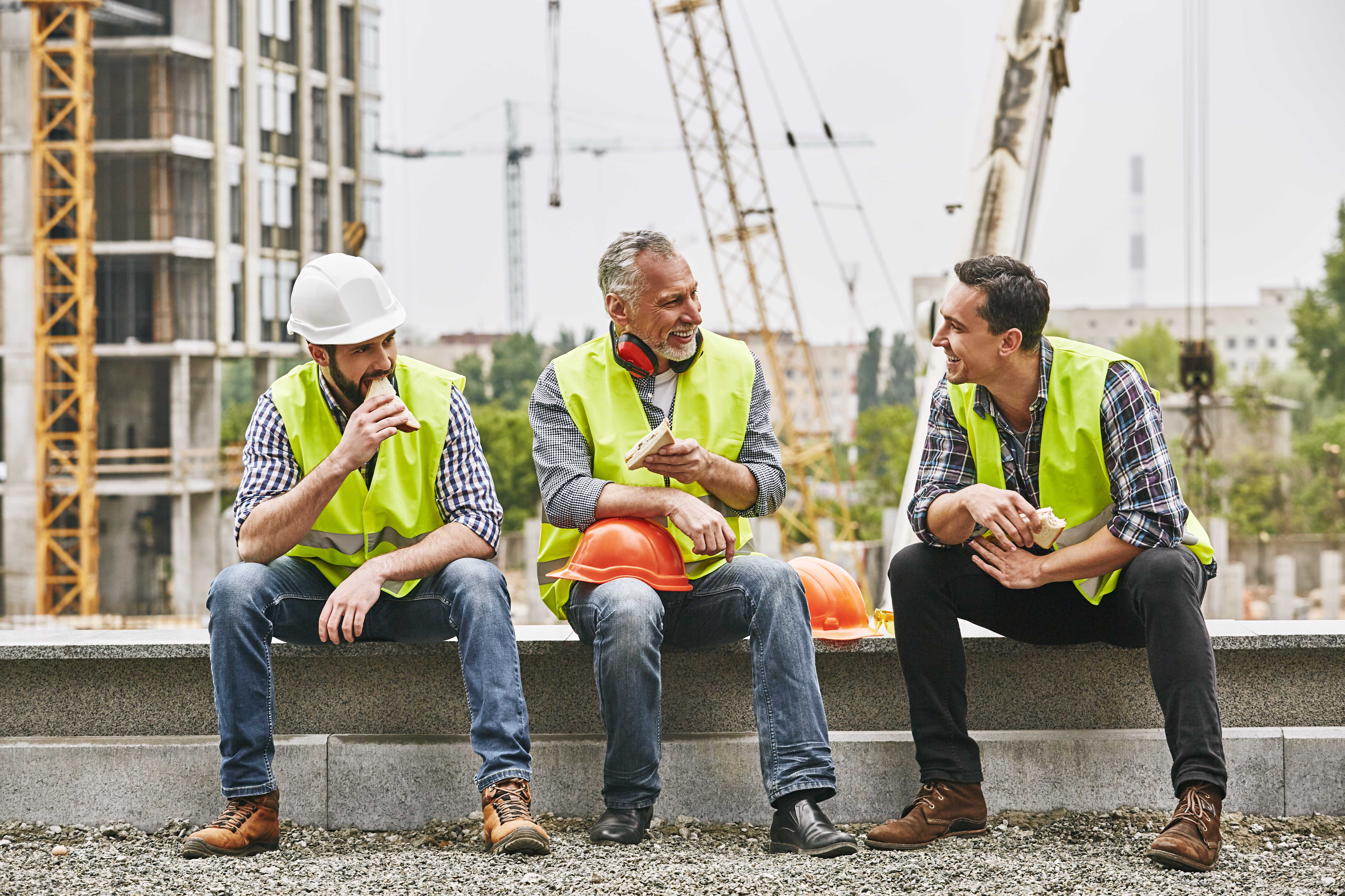 Three builders enjoying their lunch on the roof of their construction site.