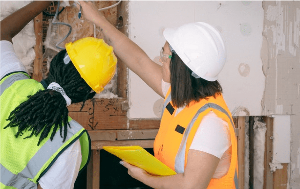 Two individuals wearing construction site safety equipment inspecting elements of a building.